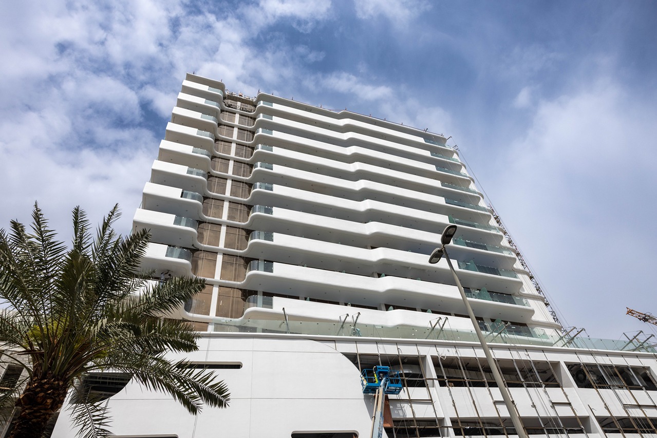 Pearl House By Imtiaz A modern white building with curved balconies, palm trees in the foreground, under a partly cloudy sky.